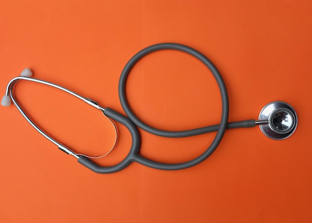 Medizinisches Stethoskop auf orangefarbenem Hintergrund auf dem Schreibtisch eines Arztes