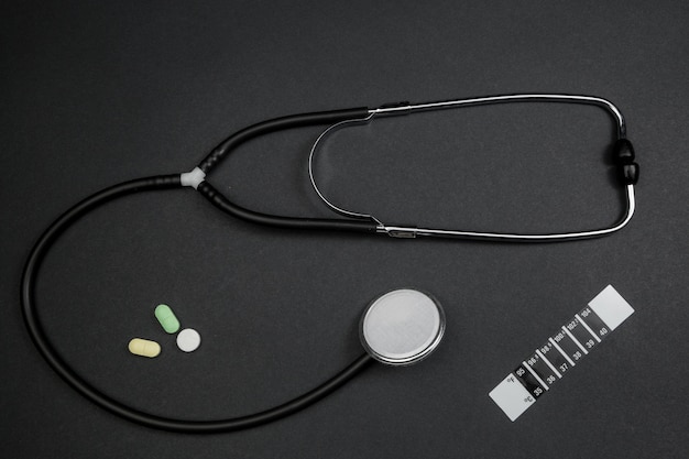 Medizinisches Stethoskop, Medikation und Thermometerstreifen auf Schwarzem lokalisierten Hintergrund