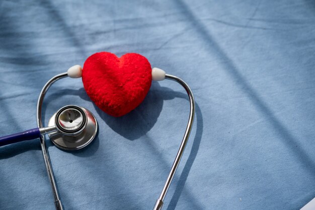 Medizinisches Stethoskop und rotes Herz auf dem Bett des Patienten.