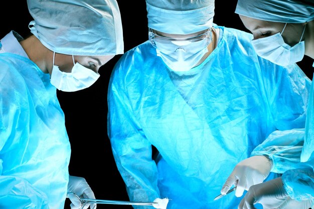 Medizinisches Team, das die Operation durchführt. Gruppe von Chirurgen bei der Arbeit im blau getönten Operationssaal.