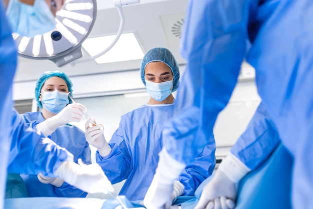 Medizinisches Team, das die Operation durchführt Gruppe von Chirurgen bei der Arbeit im Operationssaal, blau getönt Arztoperation im Operationssaal im Krankenhauskonzept für Versicherungswerbung