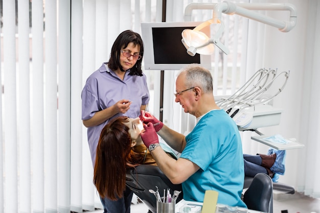 Medizinisches Zahnarztteam in der modernen Zahnarztpraxis, die Zahnbehandlung für junge Patientin tut. Leitender männlicher Zahnarzt und sein Assistent arbeiten in einer modernen Zahnklinik