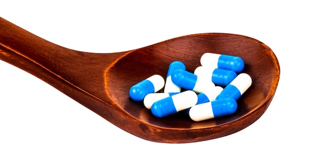 Medizinpillen, Tabletten und Kapseln auf Holzlöffel lokalisiert auf Weiß.