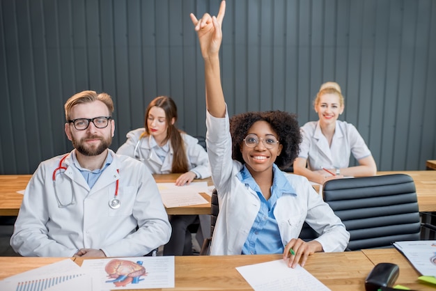 Medizinstudenten, die während des Unterrichts die Hände heben, um am Schreibtisch sitzend antworten zu wollen