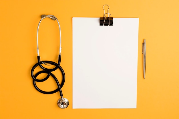 Medizinzubehör, Stethoskop, Notizblock und Stift auf Orange