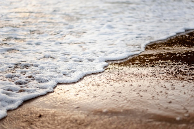 Meer, Strand, Sand, Welle, Sommer, Hintergrundkonzept. Weiße Wellen an einem Sandstrand im Sommer bei Sonnenuntergang. Hintergrund-Meer-Konzept.