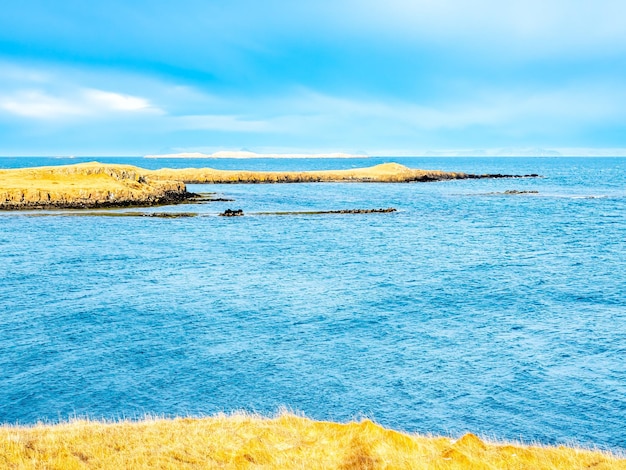 Meerblick mit Berg unter bewölktem blauem Himmel vom Stykissholmur-Leuchtturmhügel in Island