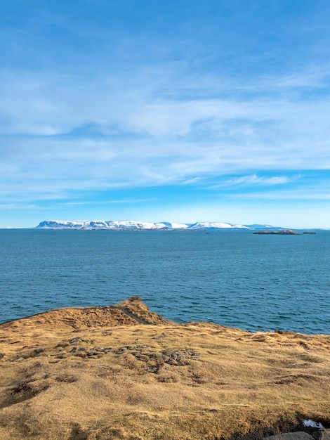 Meerblick mit Berg unter bewölktem blauem Himmel vom Stykissholmur-Leuchtturmhügel in Island