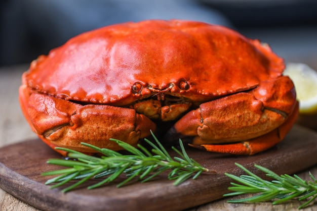 Foto meeresfrüchte schalentiere gedämpfte rote krabben oder gekochte steinkrabben - frische krabben mit zutaten zitronenrosmarin auf holzbrett