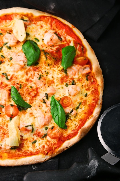 Meeresfrüchtepizza mit Garnelen und Tomaten auf dunkler Tischplatte und Pizzamesser.