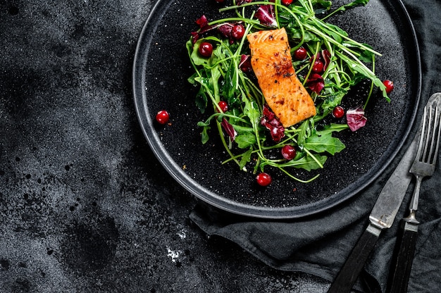 Meeresfrüchtesalat mit Lachs, Rucola, Salat und Preiselbeeren. Schwarzer Hintergrund