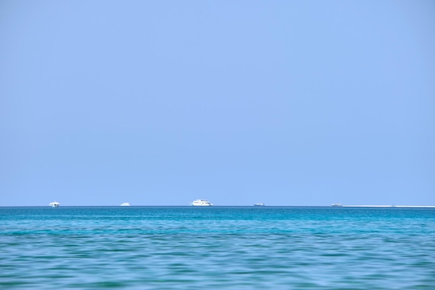 Meereslandschaft mit welliger Oberfläche aus blauem Meerwasser mit entfernten Schiffen, die auf ruhigen Wellen schwimmen