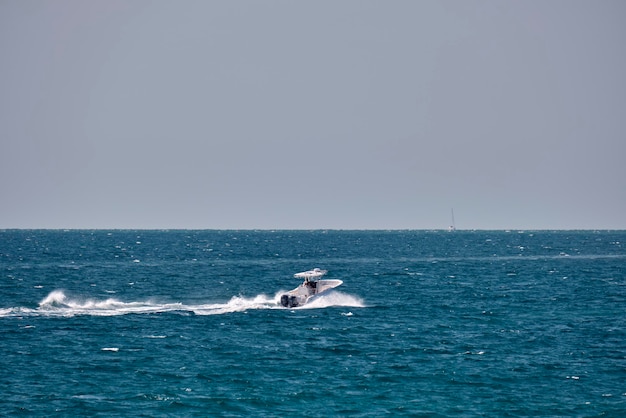 Meereslandschaft mit welliger Oberfläche aus blauem Meerwasser mit weißem Schnellboot, das schnell auf ruhigen Wellen schwimmt