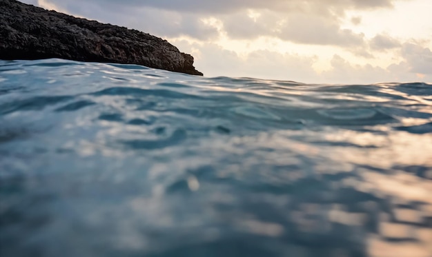 Meeresoberfläche mit verschwommenem Klippen- und Himmelshintergrund, abstrakte Nahaufnahme aus der Sicht der schwimmenden Person