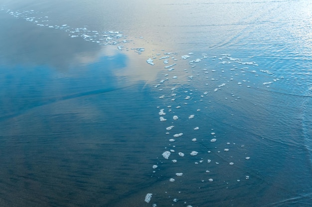 Meeresstrand mit einer zurückkommenden Welle, in der sich der Himmel spiegelt