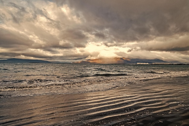 Meereswellen am Sandstrand in Reykjavik, Island Meereslandschaft mit grauem Wasser am bewölkten Himmel Kraft der Natur Fernweh oder Reisen und Urlaub