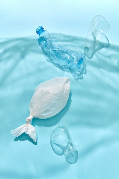 Meereswellen aus Schatten der Polyethylenfolie mit schwimmenden Flaschen, Plastikfischen und Bechern unter Wasser auf einer pastellblauen Wand, Kopienraum. Konzept der Umweltverschmutzung des Weltozeans.