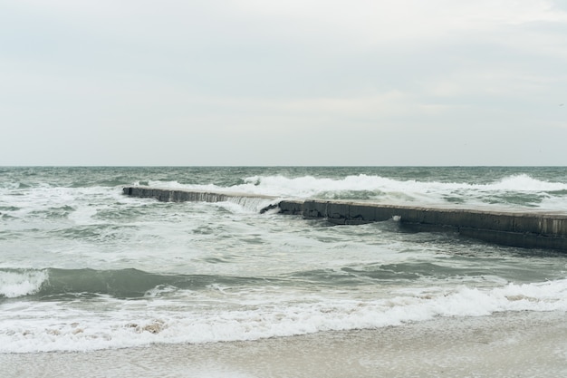 Meereswellen, die am bewölkten Tag des konkreten Wellenbrechers brechen