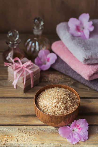 Meersalz natürliche handgemachte Seife Naturkosmetiköl und bunte Handtücher mit Azaleenblumen auf rustikalem Holzhintergrund