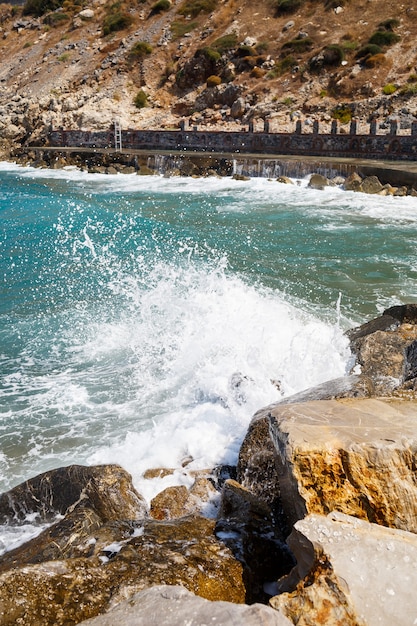 Meerwasser schlägt gegen felsige Felsen und schlägt Wellen mit Schaum, zerklüfteter Pier im Meer