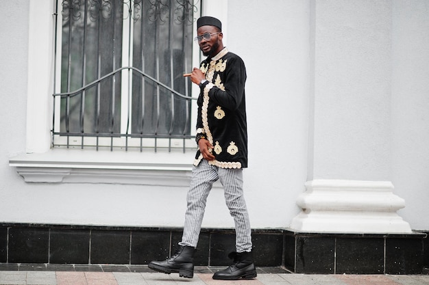 Mega stylischer afrikanischer Mann in traditioneller Jackenhaltung. Modischer schwarzer Typ mit Hut und Sonnenbrille mit Zigarre in der Hand.