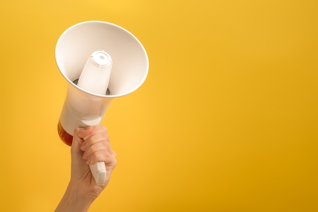 Megáfono en manos de mujer sobre un fondo amarillo. Copie el espacio.