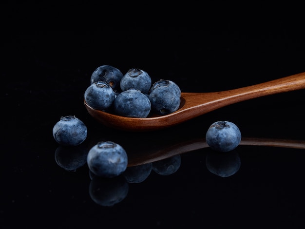 Mehrere Blaubeeren in einem Holzlöffel auf einem schwarzen glänzenden Hintergrund