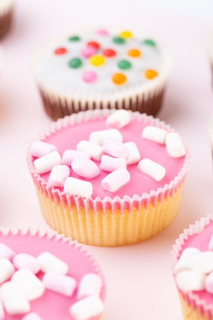 Mehrere bunte schön dekorierte Muffins auf einer rosa Oberfläche, Draufsicht.