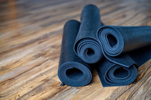 Mehrere gerollte Yoga oder Fitness Gummimatten schwarze Farbe auf Holzboden. Sportzubehör