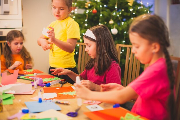 Mehrere Grundschulkinder während des Prozesses der Erstellung von Weihnachtskarten mit Wintergrüßen Verbringen Winterabende zusammen, um Papier-Öko-Geschenke zu erstellen