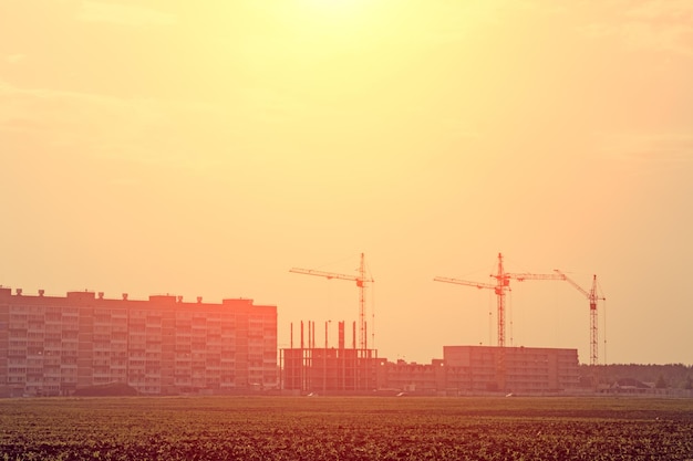 Mehrere im Bau befindliche Häuser und ein Kran auf einem Hintergrund des Himmels mit der abgehenden Sonne