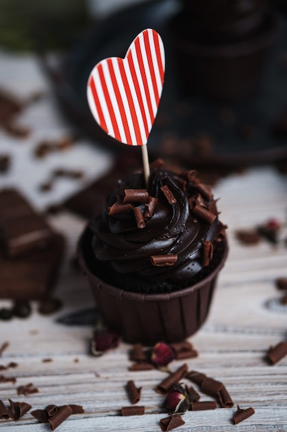 Mehrere Muffins oder Cupcakes mit schokoladenförmiger Sahne am weißen Tisch. Eine Weihnachtskarte in Form eines Herzens zum Valentinstag in einem von ihnen.