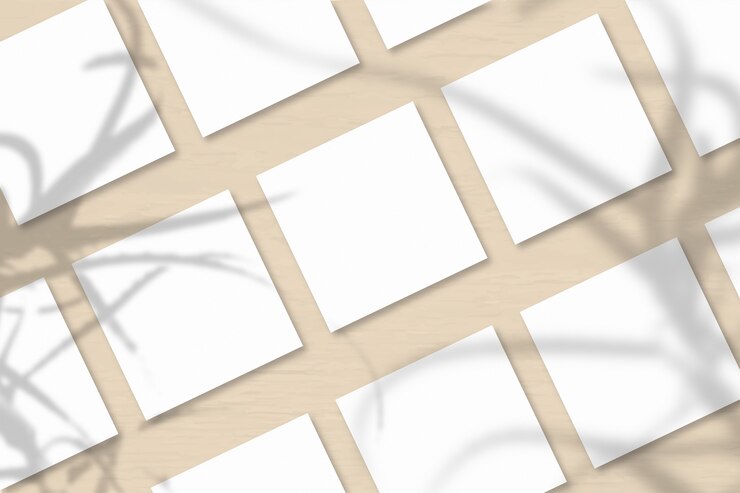 Mehrere quadratische Blätter aus weißem strukturiertem Papier vor einem orangefarbenen Wandhintergrund. Modell mit einer Überlagerung von Pflanzenschatten. Natürliches Licht wirft Schatten von der Aloe. Horizontale Ausrichtung