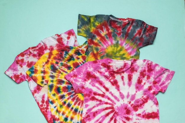 Mehrere T-Shirts im Tie-Dye-Stil auf blauem Grund. Flach liegen.