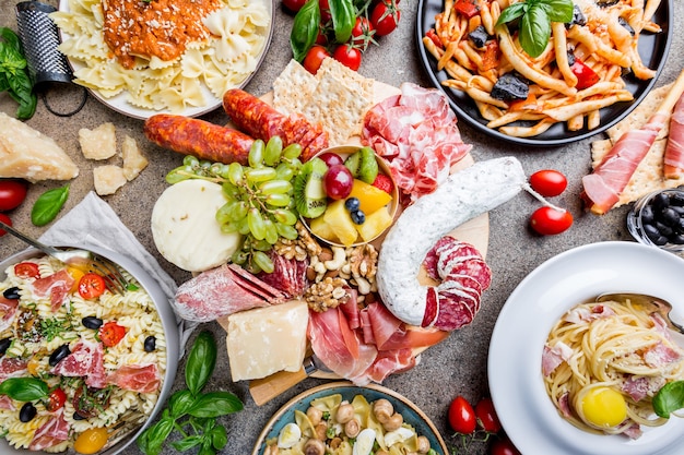 Mehrere Teller Pasta mit verschiedenen Saucen und verschiedenen Snacks und Vorspeisen auf Stein.