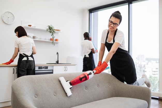 Foto mehrethnisches weibliches staubsauger-sofa mit tragbaren schnurlosen staubsaugern