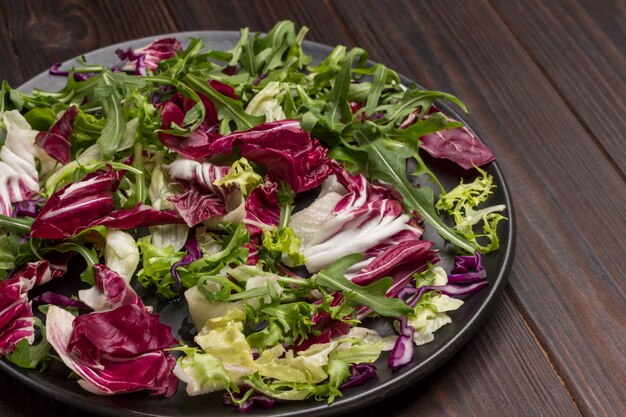 Mehrfarbige Blattgemüsemischung in schwarzer Platte. Veganes Essen. Natürliches Heilmittel zur Stärkung der Immunität. Draufsicht. Nahansicht.