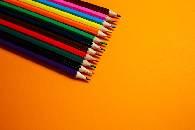 Mehrfarbige Bleistifte zum Zeichnen auf einem orangefarbenen Hintergrund gestapelt. Schreibwaren