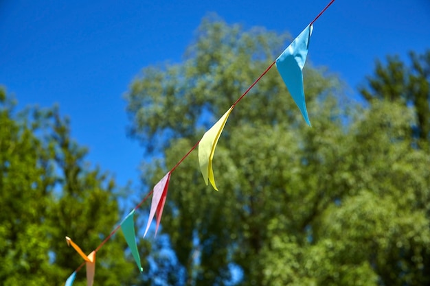 Mehrfarbige dreieckige Papierfestivalflaggen auf blauem Himmel und grünen Bäumen