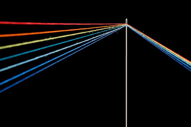 Mehrfarbige Fäden zum Nähen in Form eines Regenbogens verlaufen durch eine antike Nadel auf schwarzem Hintergrund