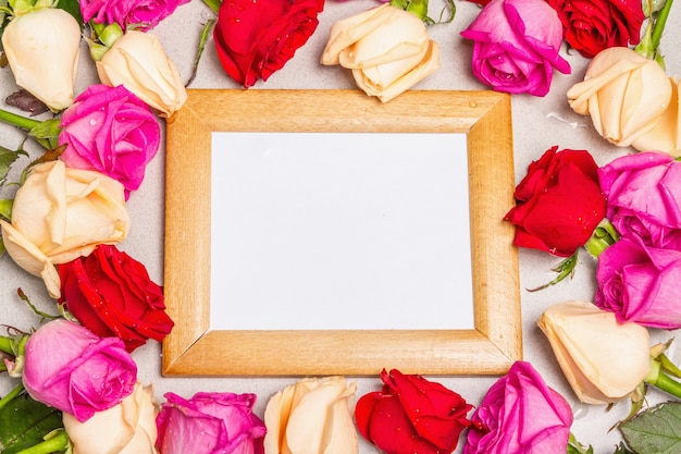 Foto mehrfarbige frische rosen und ein holzrahmen auf hellem steinhintergrund. festliches geschenk, grußkarte für ostern, geburtstag, valentinstag oder hochzeit. urlaubskonzept, ein platz für text