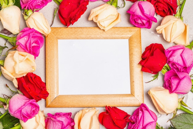 Mehrfarbige frische Rosen und ein Holzrahmen auf hellem Steinhintergrund. Festliches Geschenk, Grußkarte für Ostern, Geburtstag, Valentinstag oder Hochzeit. Urlaubskonzept, ein Platz für Text