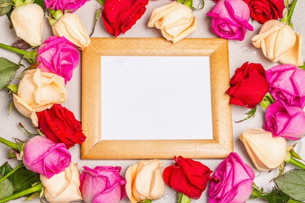 Mehrfarbige frische Rosen und ein Holzrahmen auf hellem Steinhintergrund. Festliches Geschenk, Grußkarte für Ostern, Geburtstag, Valentinstag oder Hochzeit. Urlaubskonzept, ein Platz für Text