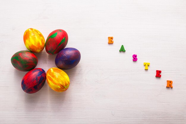 Mehrfarbige Holzbuchstaben, aus denen die Worte Frohe Ostern und dekorative bunte Eier auf weißem Hintergrund bestehen.