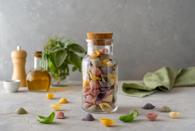 Mehrfarbige italienische Pasta Conchiglie oder Muscheln in Olivenöl aus Glasflaschen. Konkreter Hintergrund