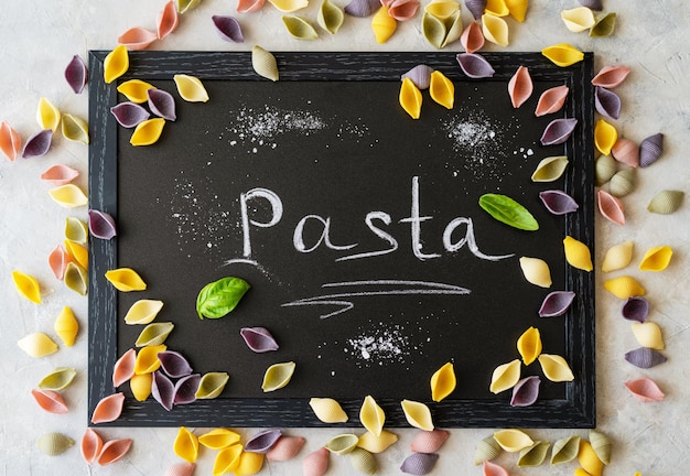 Mehrfarbige italienische Pasta Conchiglie oder Muscheln mit Basilikumblättern auf Kreidetafel Word Pasta