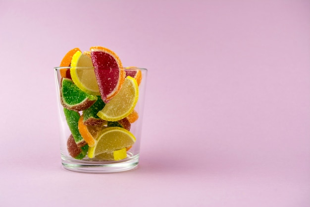 Mehrfarbige Marmelade in Form von Zitrusfruchtscheiben in einem transparenten Glas auf einem rosa Hintergrund