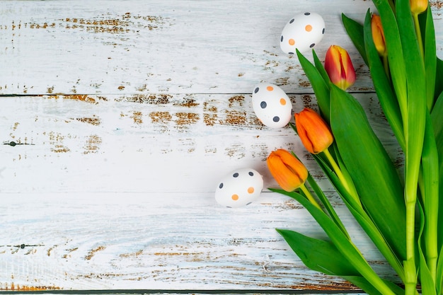 Mehrfarbige Ostern bemalte gesprenkelte Eier im Korb auf weißem Holztisch mit Tulpen