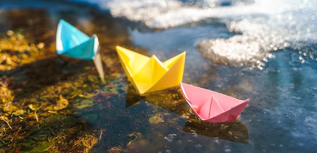 Foto mehrfarbige papierboote bunte rosa gelb blau orange schiffe in großen frühlingsschneepfützen auf der winterstraße warmes nasses regenwetter altes gras hallo frühling herbst kinder spielen viel spaß im freien