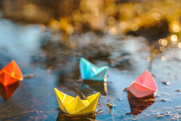 Mehrfarbige Papierboote Bunte rosa gelb blau orange Schiffe in großen Frühlingsschneepfützen auf der Winterstraße Warmes nasses Regenwetter altes Gras Hallo Frühling Herbst Kinder spielen viel Spaß im Freien